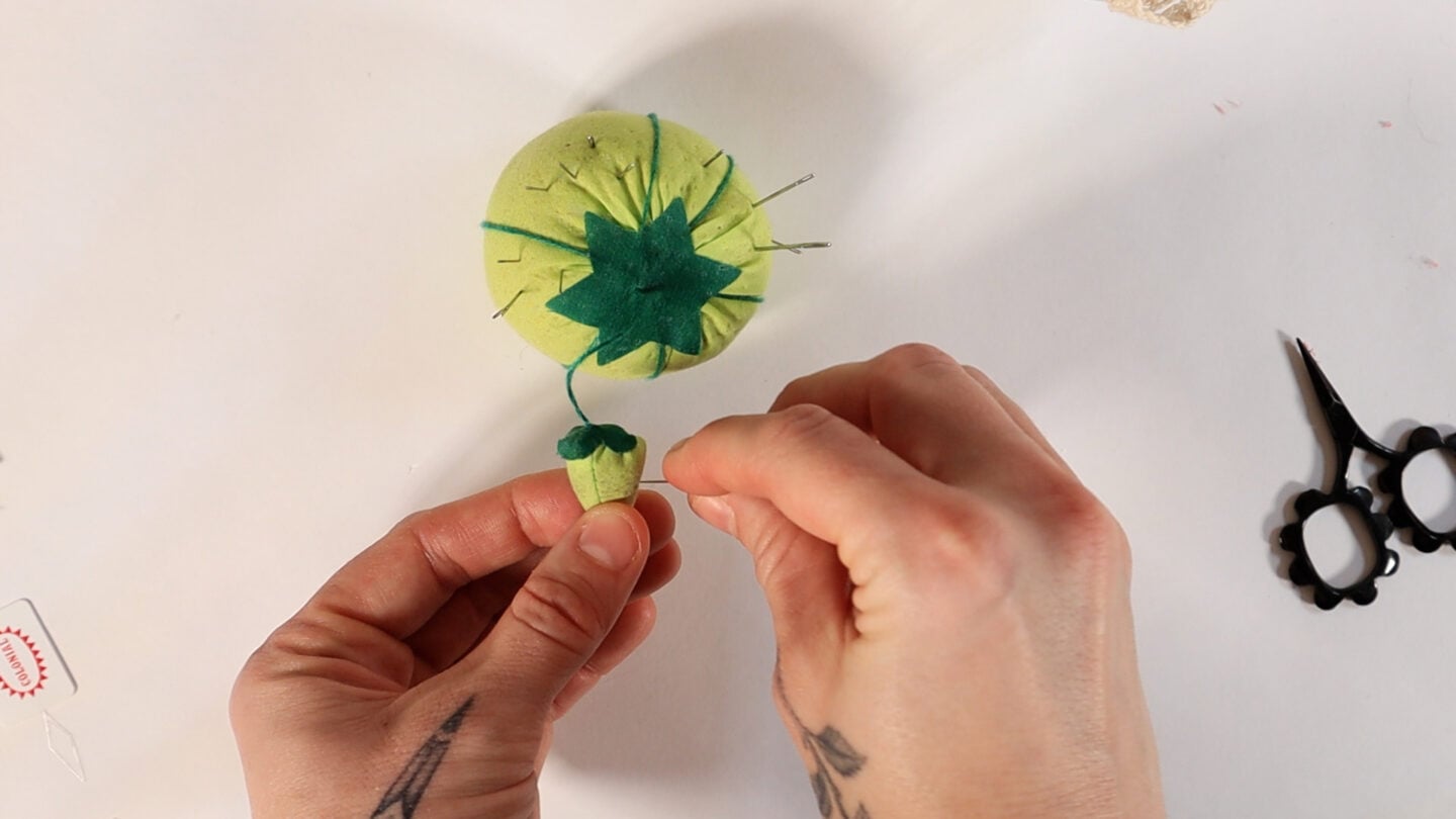 sharpening a needle through the strawberry attached to a green tomato pin cushion