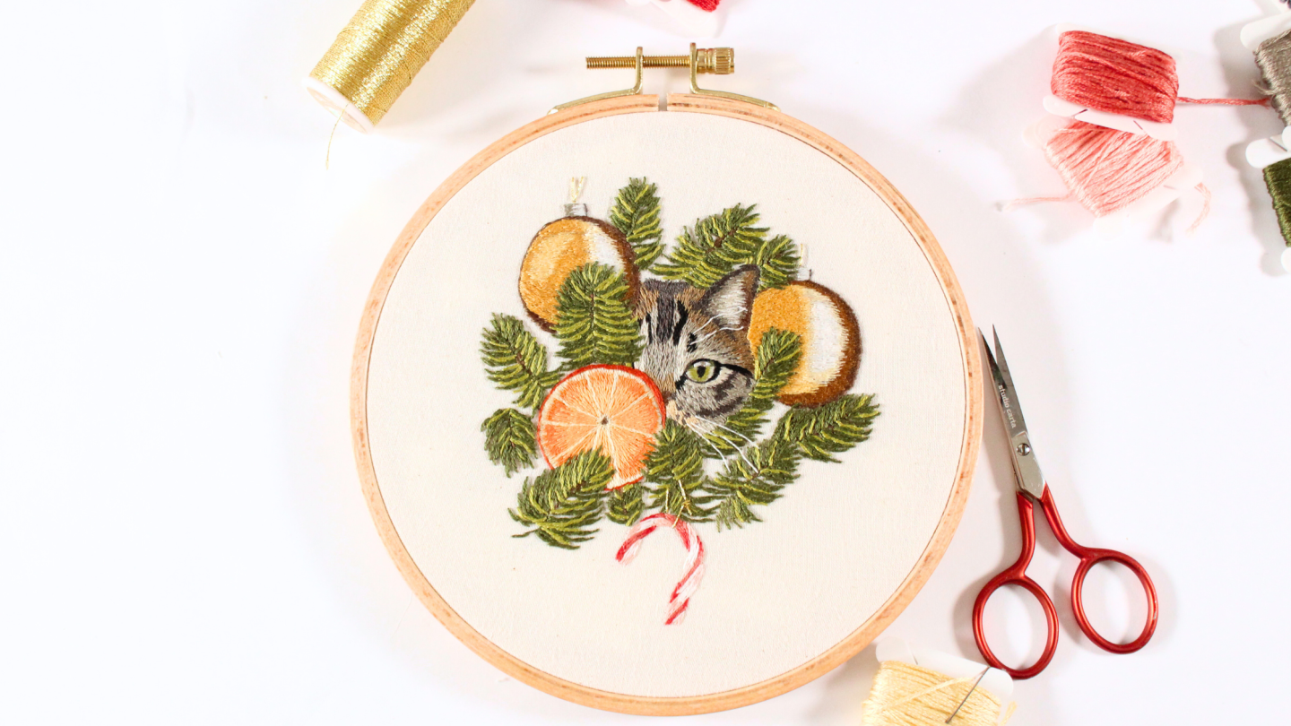embroidery of a cat peeking through the Christmas tree