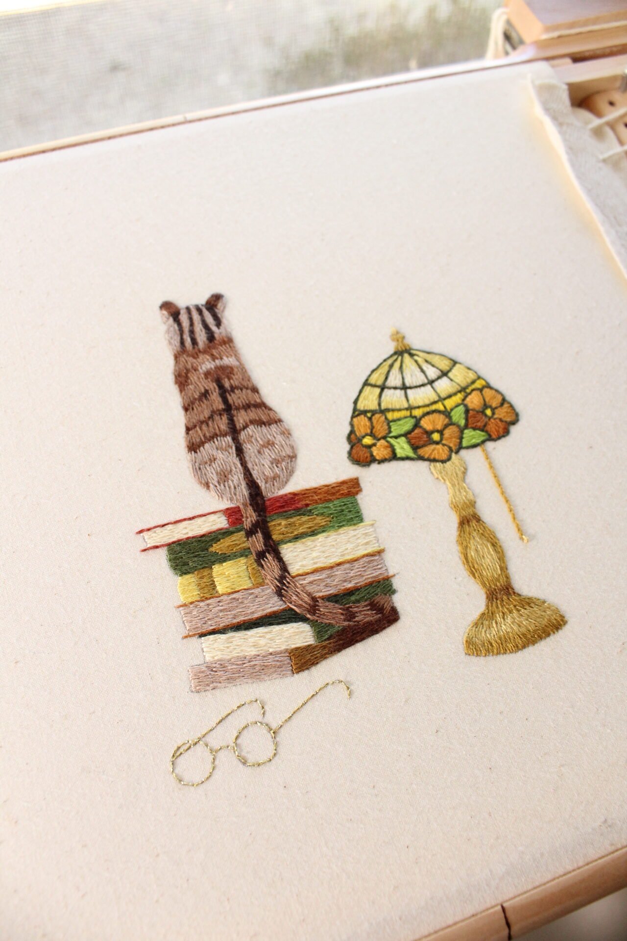 embroidery of a cat sitting on books, a stained glass lamp beside them