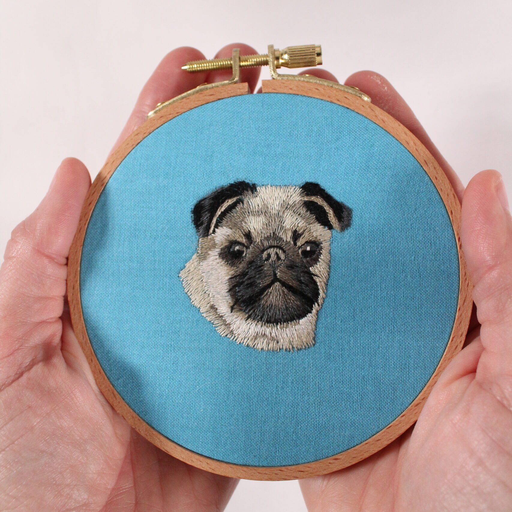 hands holding pug embroidery design on blue fabric