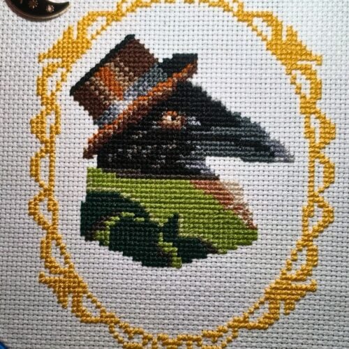 cross stitch of a raven wearing a top hat and overcoat