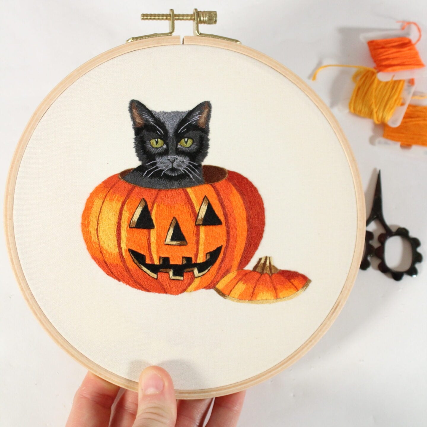 an embroidery of a black cat peeking out of the a jack o lantern