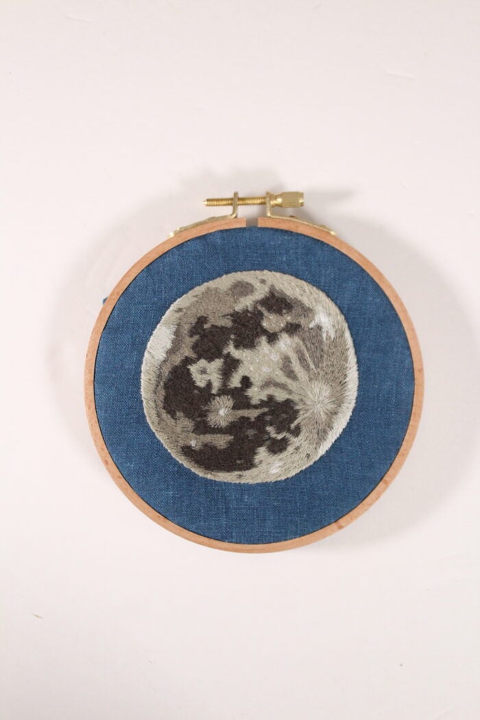 embroidery of a realistic full moon on dark blue fabric
