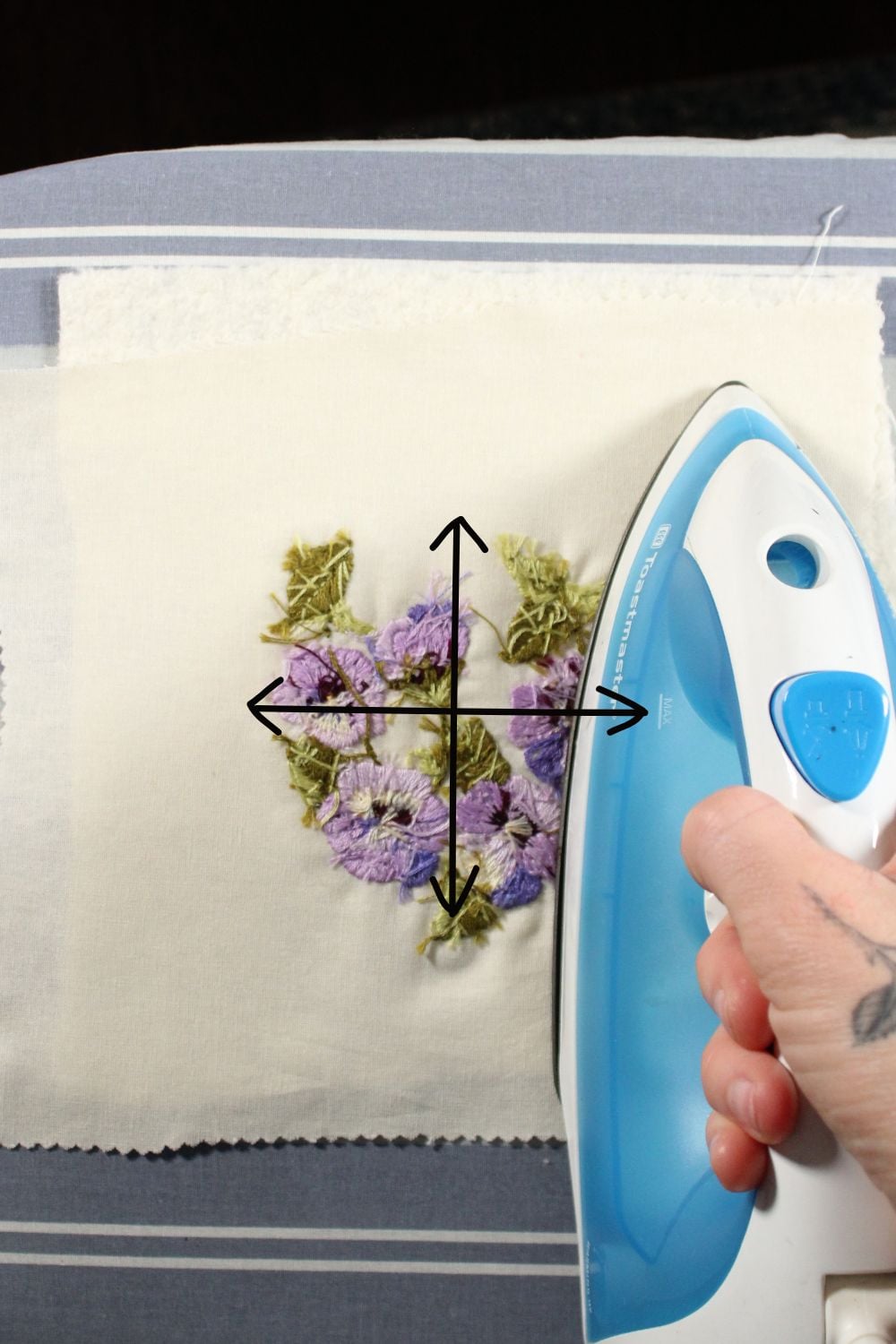 Ironing along the back of an embroidery with arrows pointing in the vertical and horizontal direction of the grain lines of the fabric