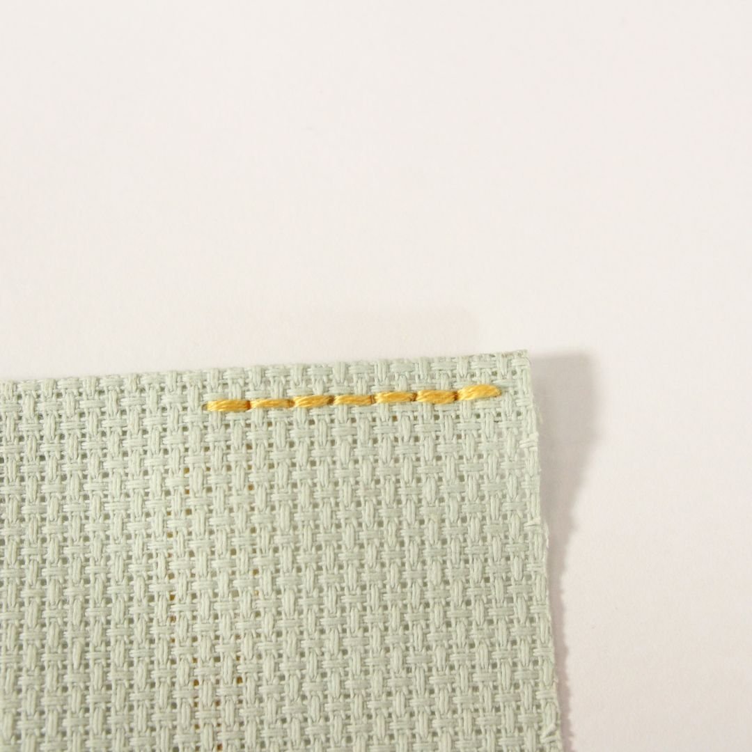 finished edge of light green Aida cloth secured with back stitches using yellow thread