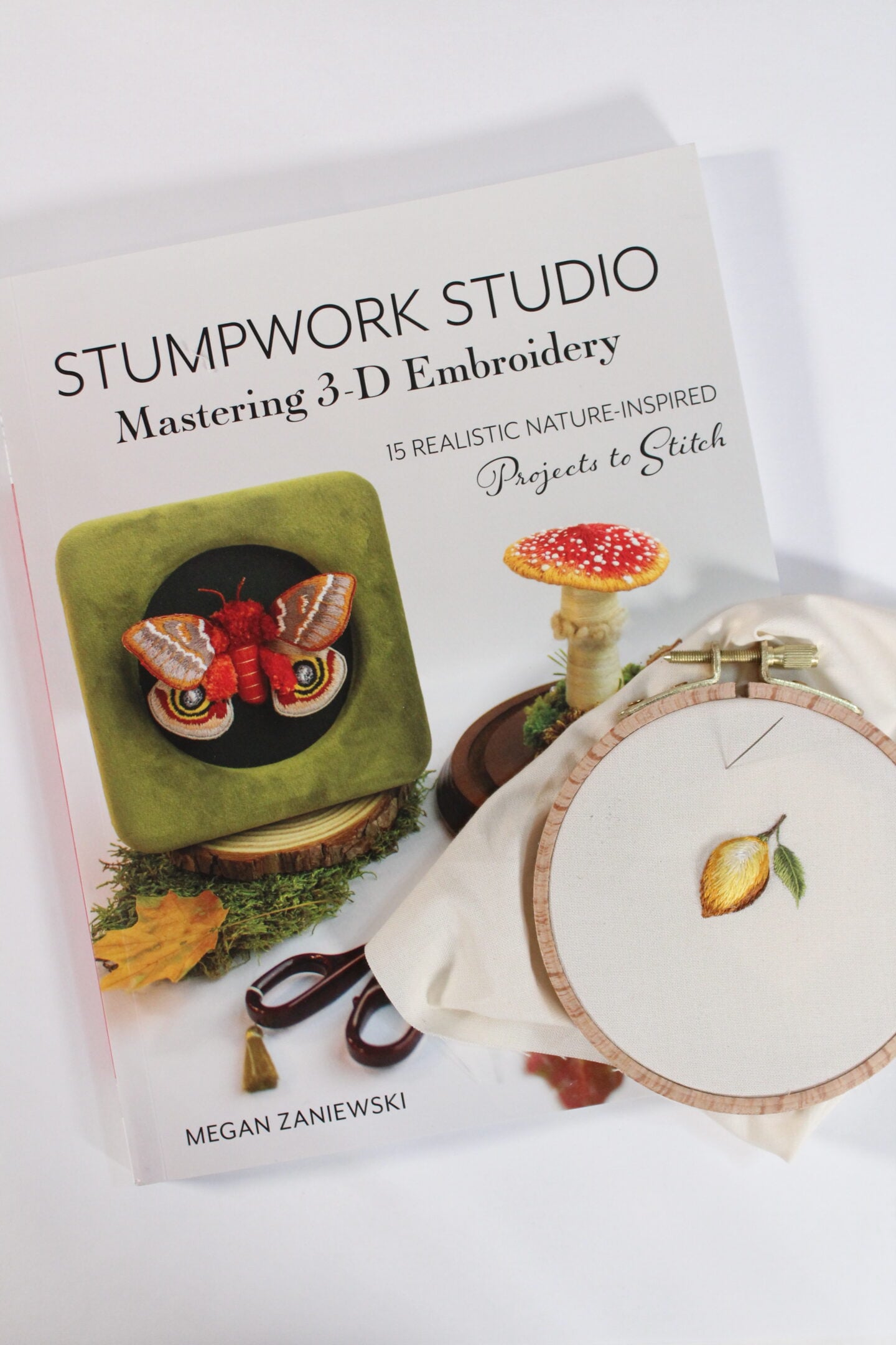 an embroidery of a 3-dimensional lemon sitting on top of the book Stumpwork Studio