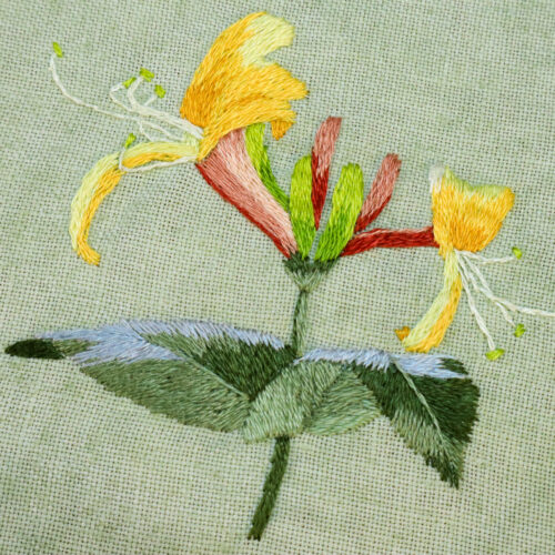 close up of embroidered honeysuckle flowers on green linen fabric