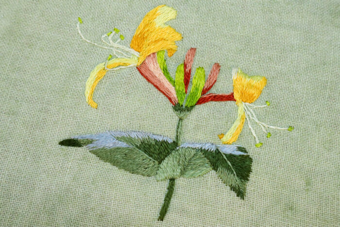 close up of embroidered honeysuckle flowers on green linen fabric