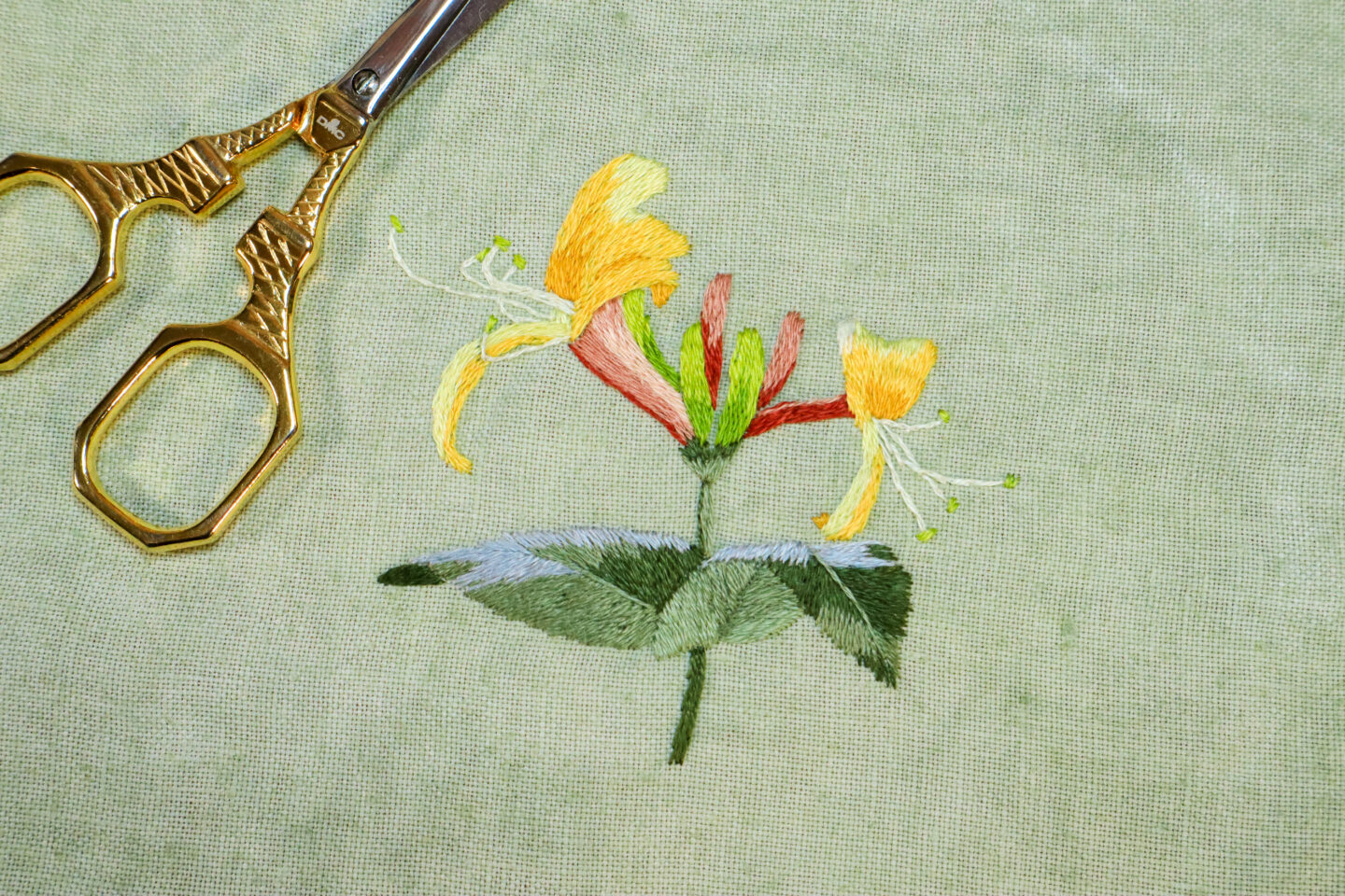 embroidery of yellow honeysuckles on green linen fabric