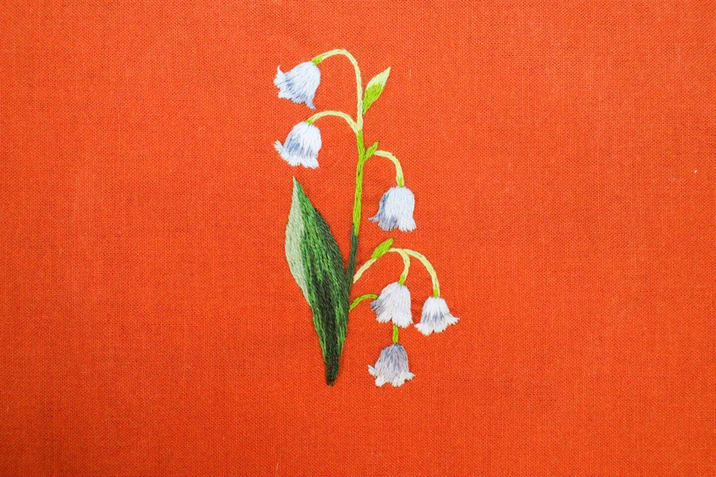 embroidery of a lily of the valley flower on red fabric