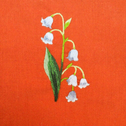 embroidery of a lily of the valley flower on red fabric