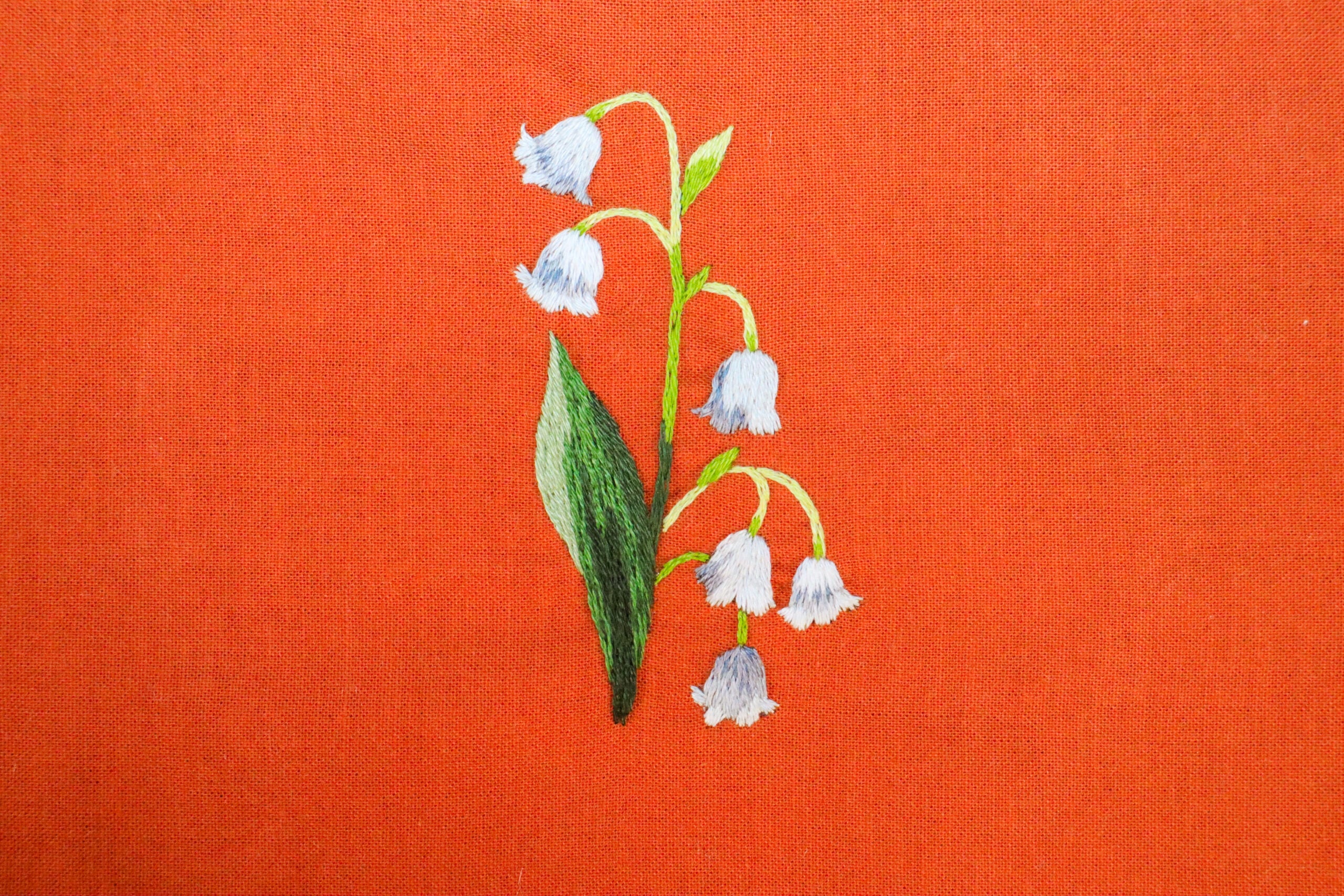 embroidery of a lily of the valley flower on red fabric