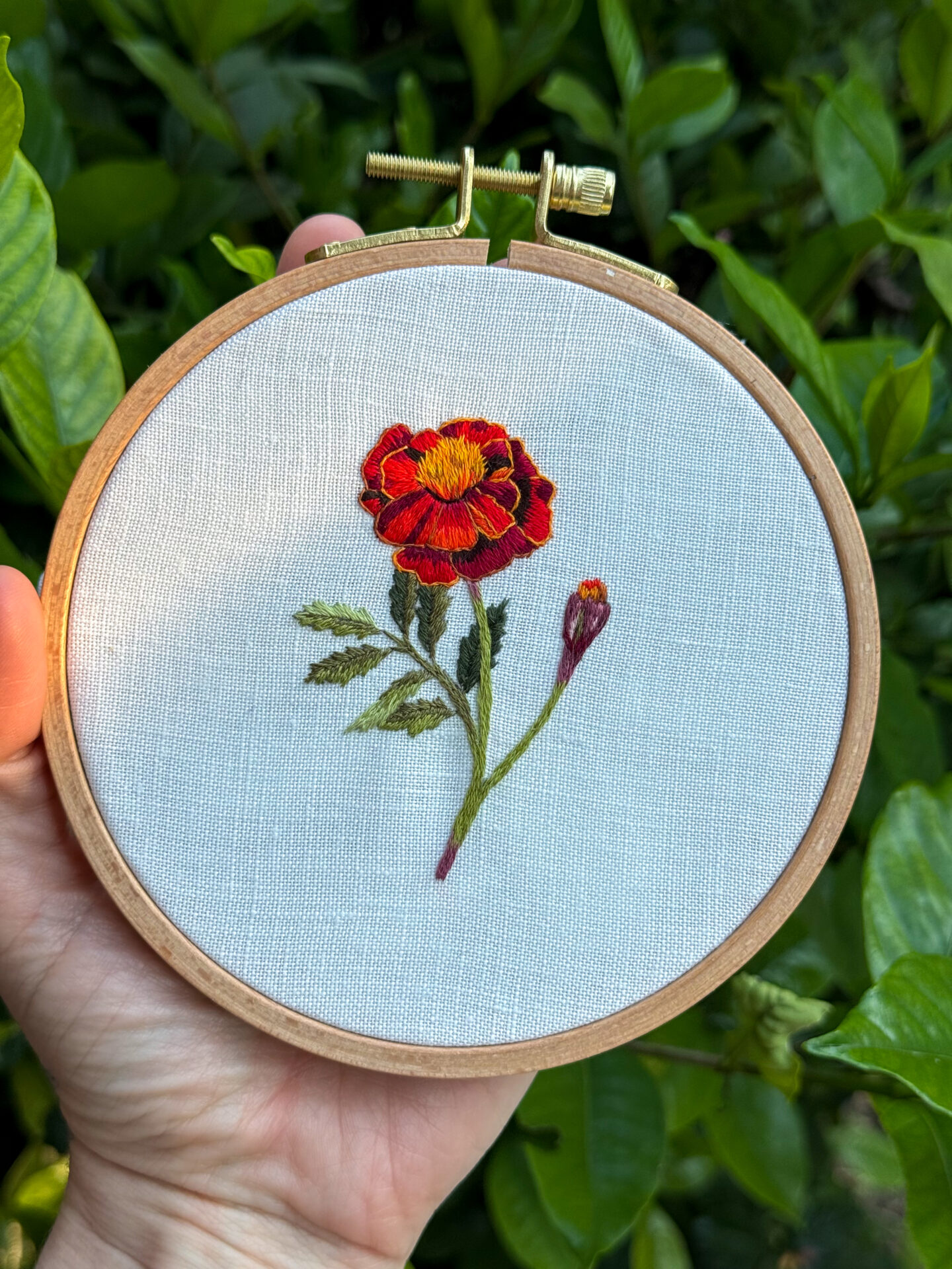 embroidery of a red marigold flower on white linen fabric