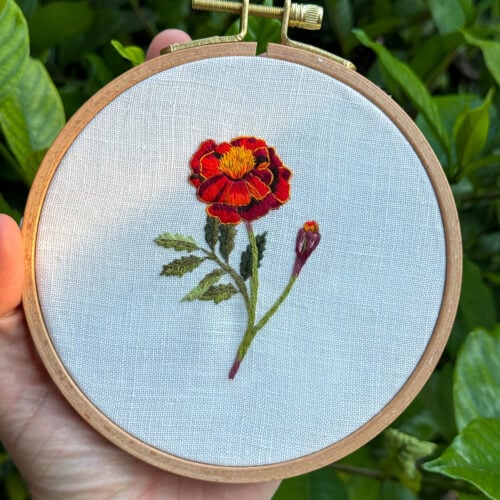 embroidery of a red marigold flower on white linen fabric